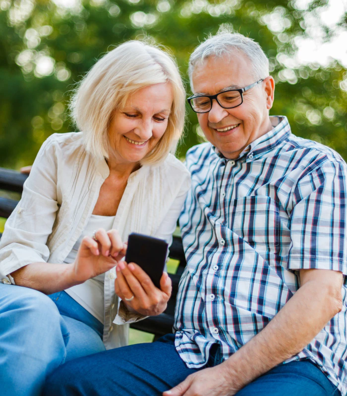 couple sitting on park bench looking at phone researching life insurance for retirement